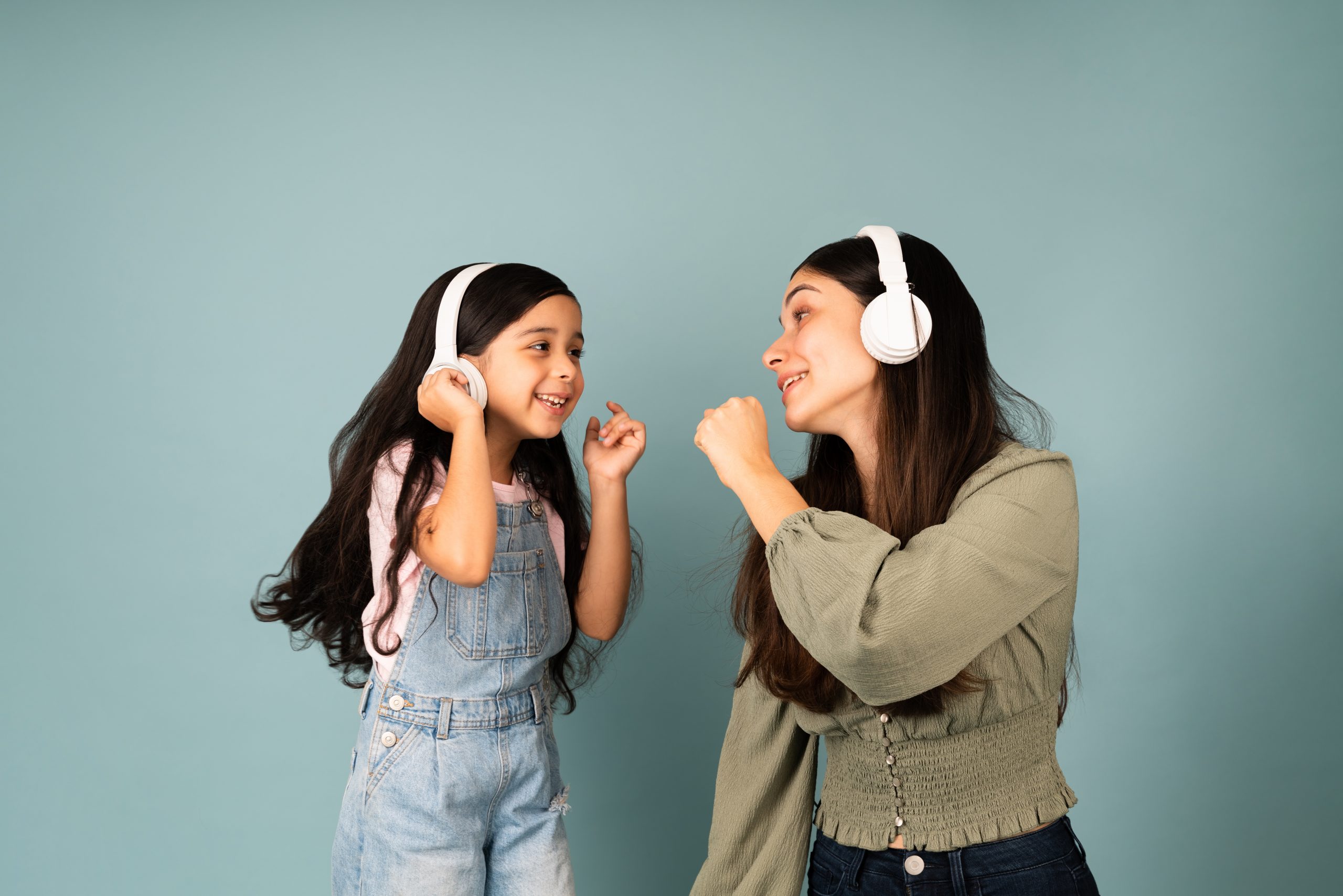 Young mom and little girl singing together while listening to Spanish songs for kids with headphones